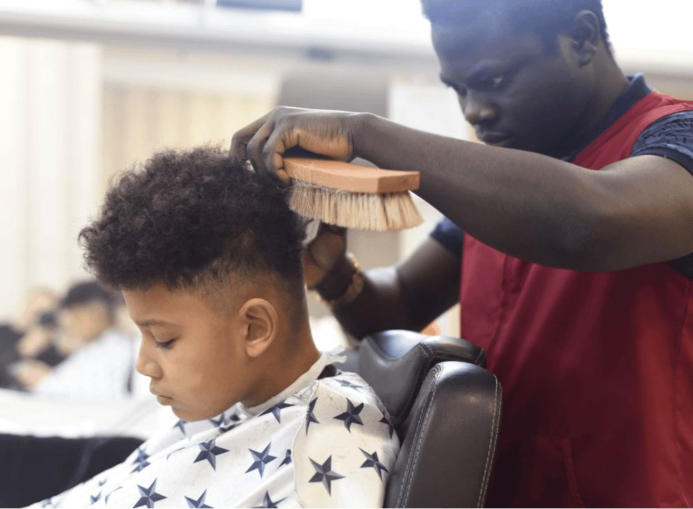 A young boy having his hair cut at the barbers.
