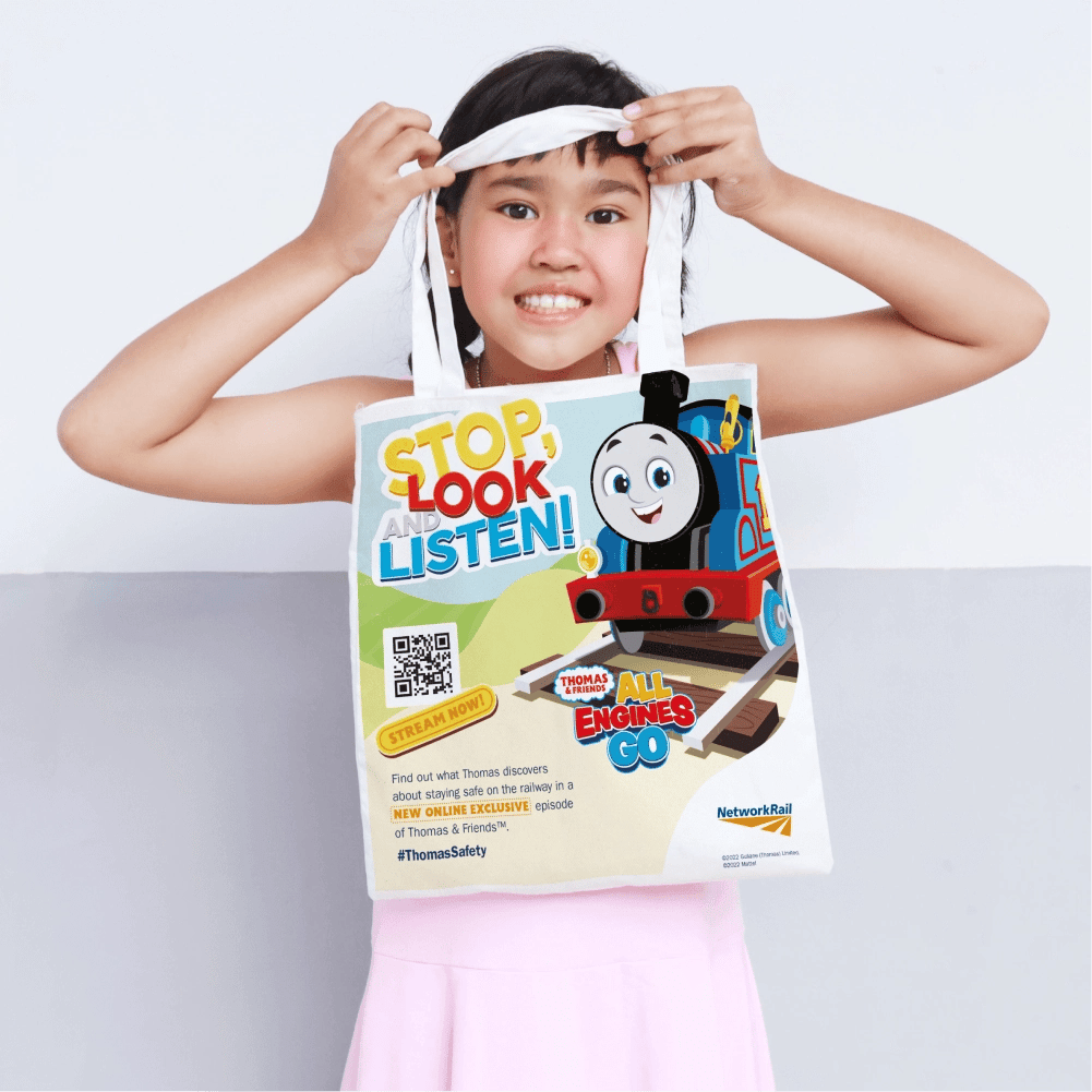 A young girl holding a tote bag with the 'stop look and listen' branding.