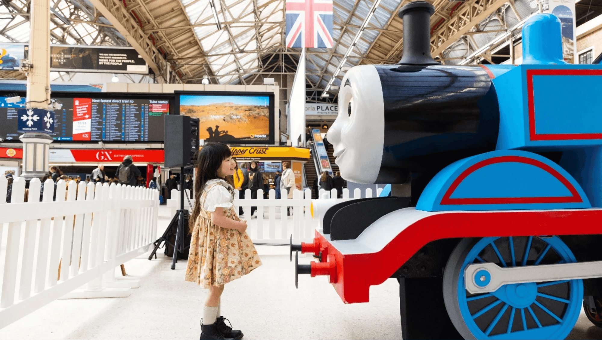 A young girl standing in a station, in front of a thomas the tank engine installation.